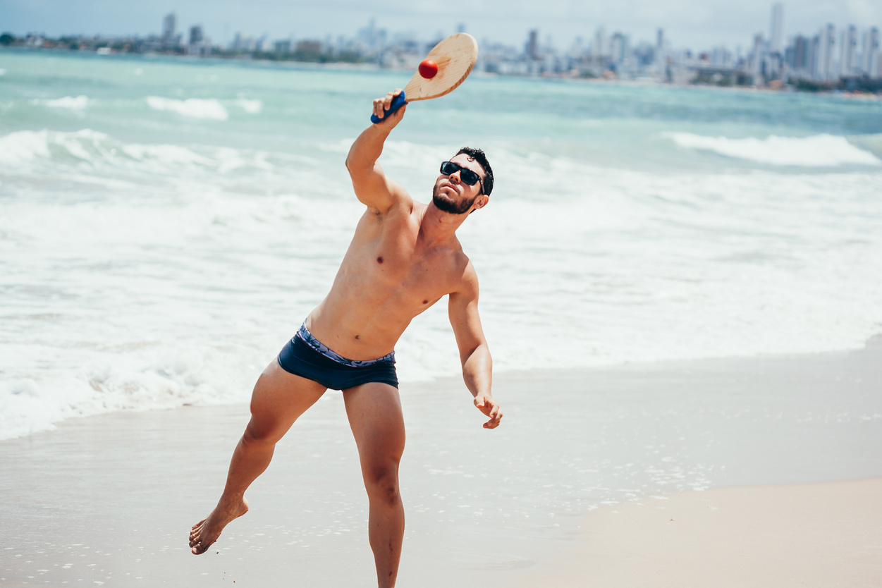 Young Brazilian man playing beach tennis on the beach with swimwear